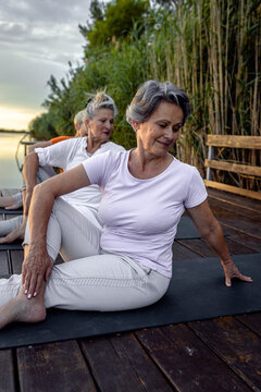 Group of senior woman doing yoga exercises by the lake.