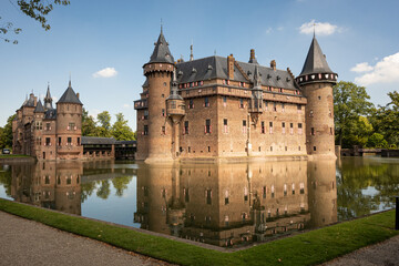Fototapeta na wymiar outside of Kasteel De Haar Dutch medieval castle reflection in moat on sunny summer day. Flowers match colour of Utrecht Netherlands where historic building with European architecture is located