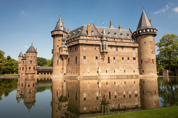 outside of Kasteel De Haar Dutch medieval castle reflection in moat on sunny summer day. Flowers match colour of Utrecht Netherlands where historic building with European architecture is located