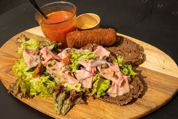 Typical Dutch lunch called twaalfuurtje meaning twelve O'Clock food served outside on a rustic chopping board. hearty filling Netherlands meal consists of croquette, bread, ham, salad and soup