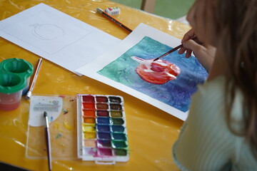 Almaty, Kazakhstan - 10.12.2022 : A teenager paints with watercolor paints at a table.