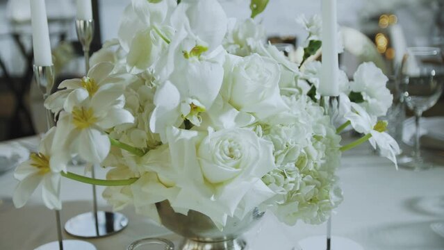 Floristic decorations at the wedding. Close-up bouquet of white flowers are on the table in the restaurant. Beautiful arrangement of flowers with a roses and candles. slow motion.