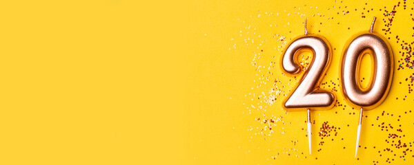 Gold candles in the form of number twenty on yellow background with confetti. 20 years anniversary...