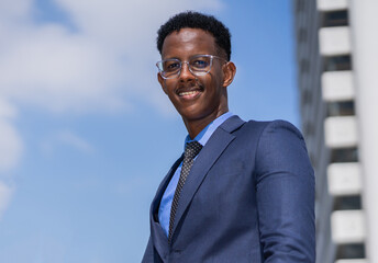 black executive man with glasses, blue suit and tie smiling and looking at camera. businessman smile, standing outside building in city with copy space