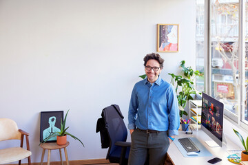 Cheerful male employee standing near table with computer