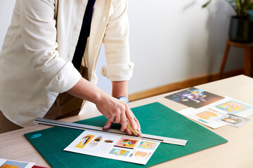 Faceless designer cutting pictures in creative workspace