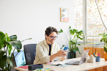 Happy entrepreneur using cellphone in creative workspace
