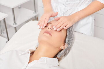 Cosmetologist massages woman face skin after rubbing moisturizing cream for rejuvenation, anti...