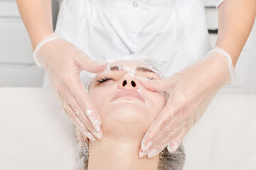 Cosmetologist massages cream mask into woman face skin for rejuvenation, anti aging skincare...