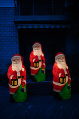 Figures of three Santa Claus at night with lamps in the yard of the house