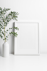 White portrait frame mockup in scandinavian room with green eucalyptus twig in vase, blank mockup