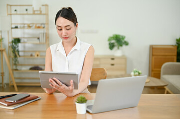 Beautiful millennial Asian businesswoman focusing on her tasks on tablet