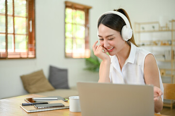 Happy Asian woman enjoys listening to music through her headphones while using computer