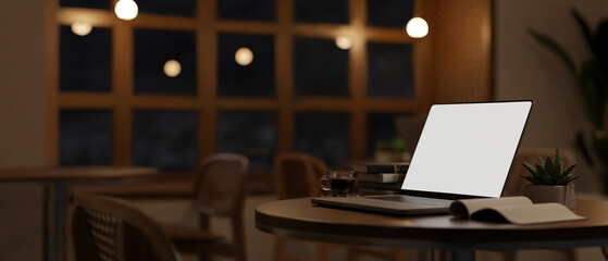 Portable laptop mockup on table in cozy and minimal coffee shop at night. workplace at night