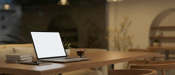 Laptop white screen mockup on wood table in minimal cozy Scandinavian coffee shop at night