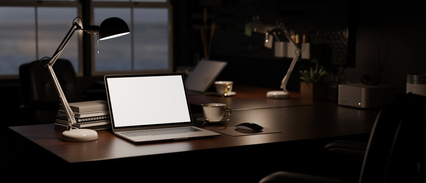 Modern dark office at night with laptop mockup, light from table lamp, and office accessories