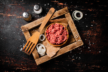 Minced meat on a wooden tray with onion rings. 