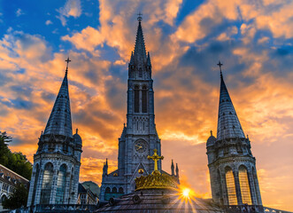 The sun star among the bell towers of the pilgrimage basilica of the apparitions of Mary in Lourdes - obrazy, fototapety, plakaty