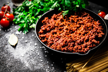 Bolognese sauce in a frying pan with pasta dry and parsley. 