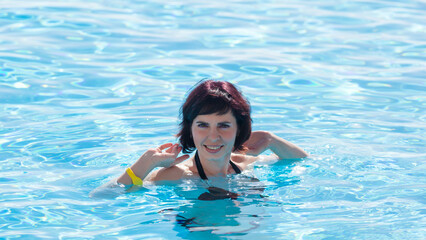 smiling adult woman is bathing in pool with clear blue water.