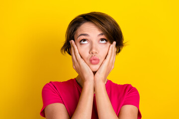 Fototapeta na wymiar Photo of dreamy funny woman dressed pink t-shirt lips pouted arms cheeks looking up empty space isolated yellow color background
