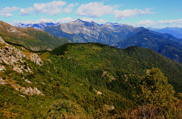 Panoramic view of the landscape with mountains and green hills in the foreground against a blue sky with clouds on Mount Cimetta, near Locarno in Switzerland