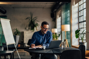 Smiling businessman working at his office, writing something in his notebook.