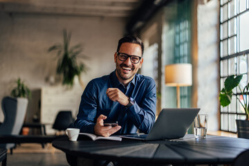 Portrait of a smiling male boss, holding a mobile phone, sitting at the office.