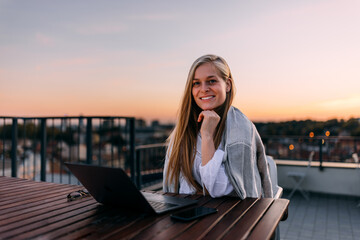 Portrait of a smiling girl, holding hands on her chin, sitting and working at the terrace.
