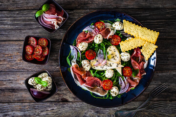 Fresh salad - prosciutto di Parma, mozzarella, pear and leafy vegetables on wooden table
