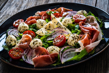 Fresh salad - prosciutto di Parma, mozzarella, pear and leafy vegetables on wooden table
