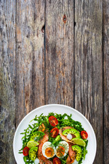 Salmon salad - smoked salmon, hard boiled eggs, avocado and leafy greens on wooden table
