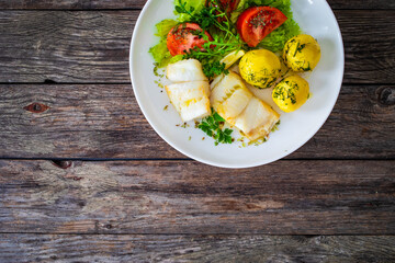 Fish dish - fried halibut with boiled potatoes and fresh vegetables on wooden table
