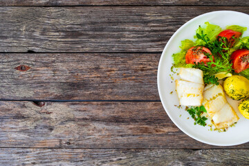 Fish dish - fried halibut with boiled potatoes and fresh vegetables on wooden table
