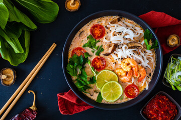 Tom Yum - Thai soup with prawns, shiitake mushrooms and noodles on wooden table
