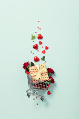 Fototapeta Valentine's day concept. Shopping trolley with gift boxes, roses, chocolate and red hearts on blue background obraz