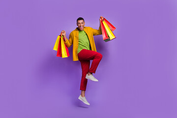 Full size photo of crazy active man jumping arms hold packages isolated on violet color background
