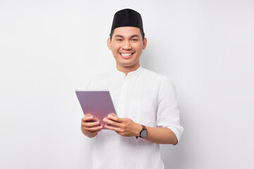 Smiling young Asian Muslim man holding digital tablet and looking at camera isolated on white background. People religious Islam lifestyle concept. celebration Ramadan and ied Mubarak
