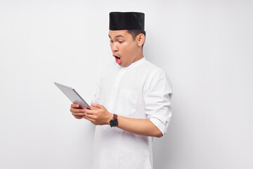 Surprised young Asian Muslim man using digital tablet and reacting to online news isolated on white background. People religious Islam lifestyle concept. celebration Ramadan and ied Mubarak