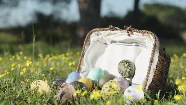 A wicker basket is lying on a meadow of yellow flowers in the forest, eggs are all scattered on the grass. Tilt