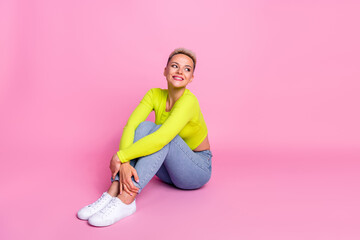 Full size photo of attractive young woman sit hug knees look empty space dressed stylish yellow outfit isolated on pink color background