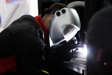 industrial worker in helmet welds steel workpieces