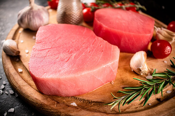 Raw tuna on a cutting board with garlic, tomatoes and spices. 