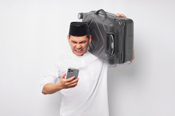 angry young Asian Muslim man carrying a suitcase and using mobile phone while reacting to bad news isolated on white background. Ramadan and eid Mubarak concept