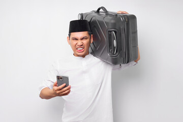 angry young Asian Muslim man carrying a suitcase and using mobile phone while reacting to bad news isolated on white background. Ramadan and eid Mubarak concept
