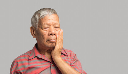 Senior man suffering from a toothache while standing on a gray background