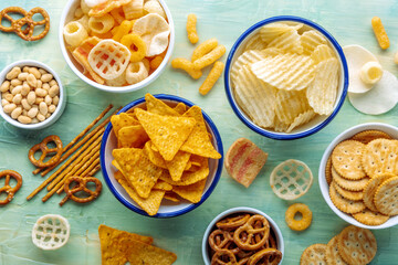 Salty snacks. Party food on a blue background. Potato and tortilla chips, crackers and other appetizers in bowls, overhead flat lay shot