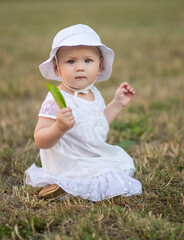 Portrait of a cute girl on the background of the nature of the park, the child sits in the grass. Looking into the camera. Lovely happy baby face. Vertical frame.
