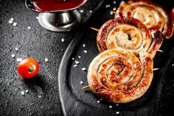 Round grilled sausages on a tray with tomato sauce.