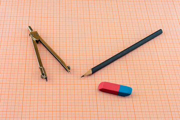 Compasses, pencil and eraser lying on a sheet of graph paper